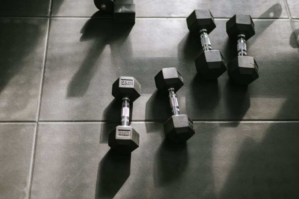 Hexagonal dumbbells on a gym floor bathed in natural sunlight, creating dynamic shadows.