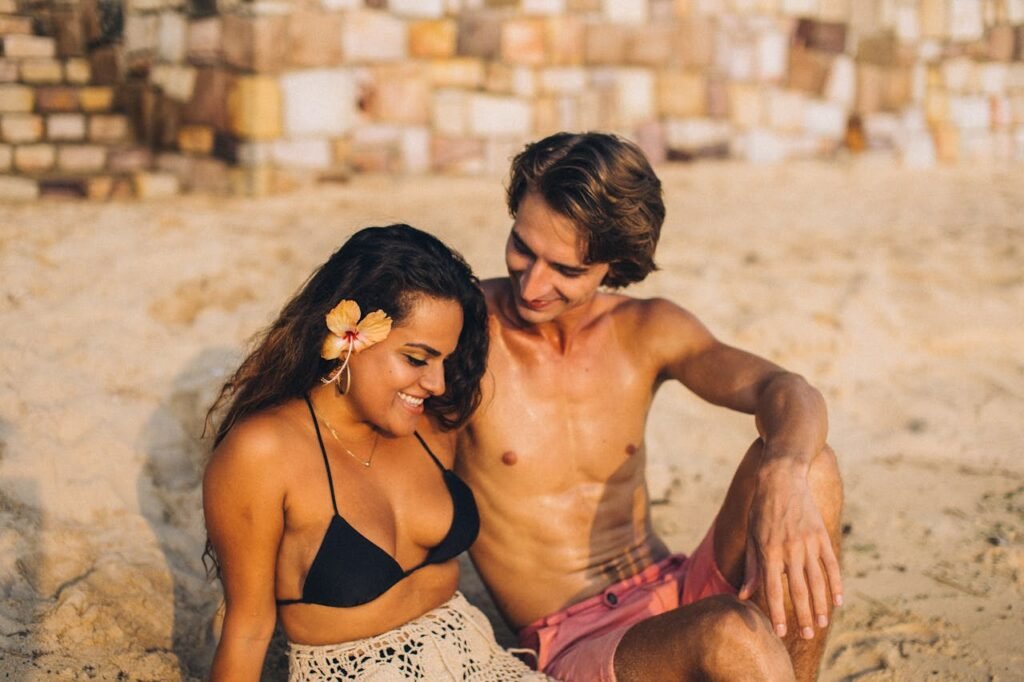 A shirtless man and woman in swimwear enjoying a sunny day on a sandy beach.