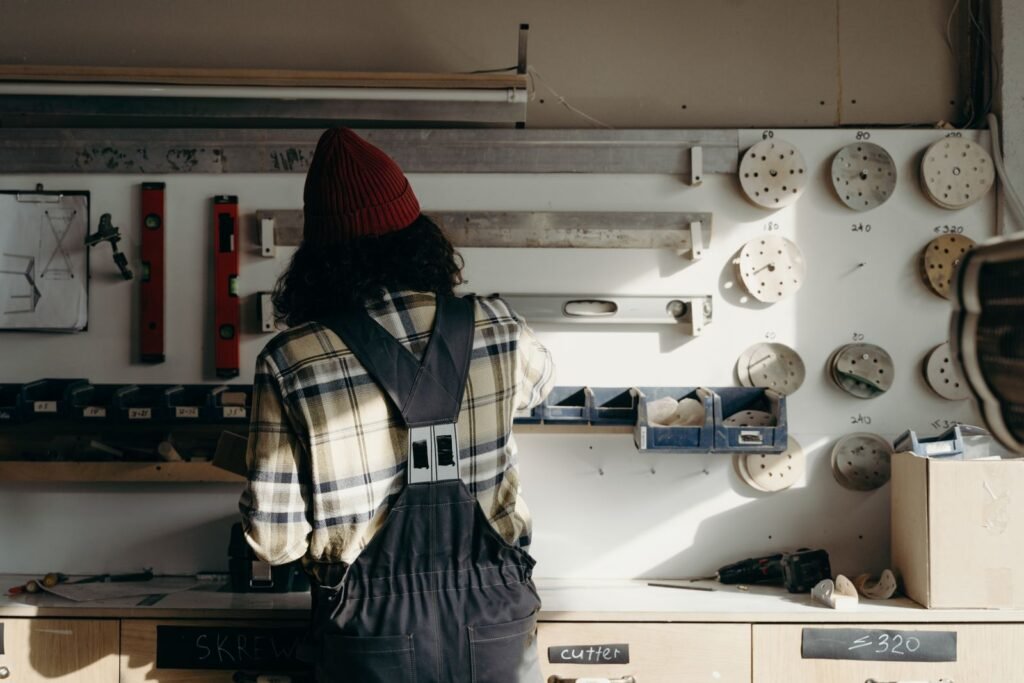 Man in a beanie and plaid shirt working at a tool wall in a home workshop