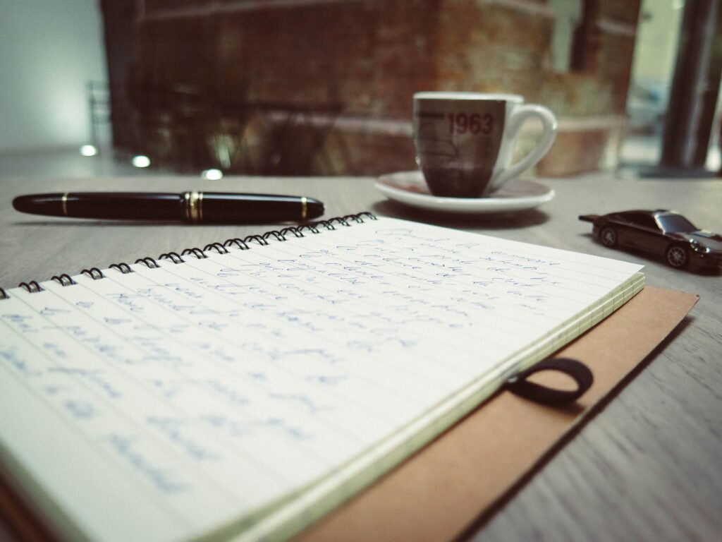Open notebook with handwritten notes, a fountain pen, and a cup of coffee on a work desk