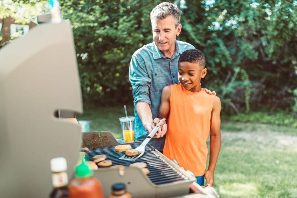 Father teaching his son to grill burgers in the backyard