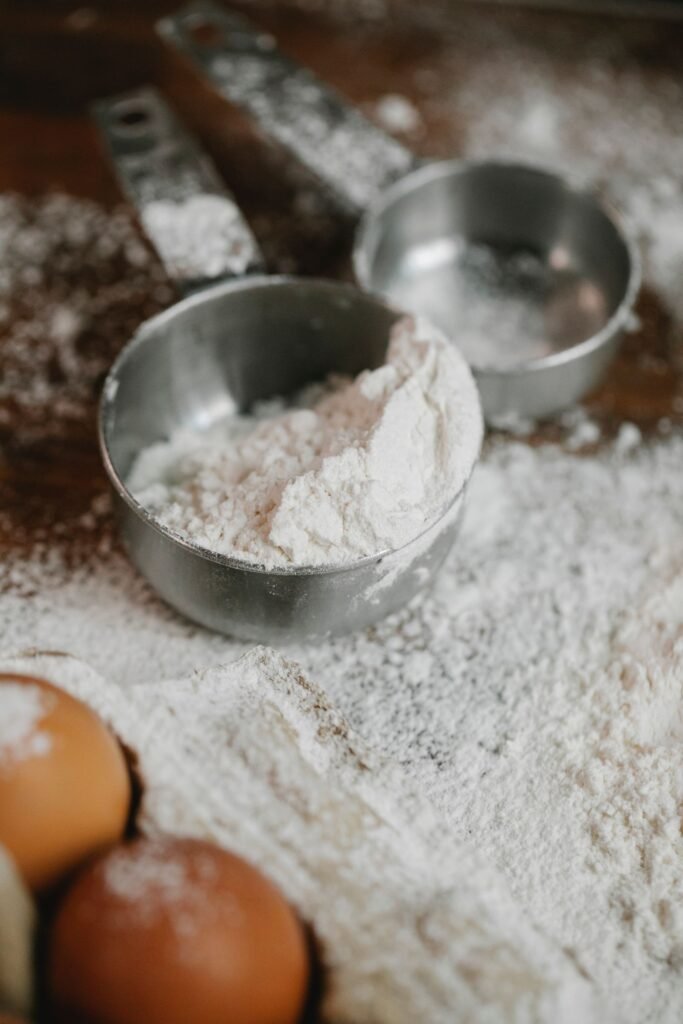 Flour in metal measuring bowls with eggs on a floured kitchen counter