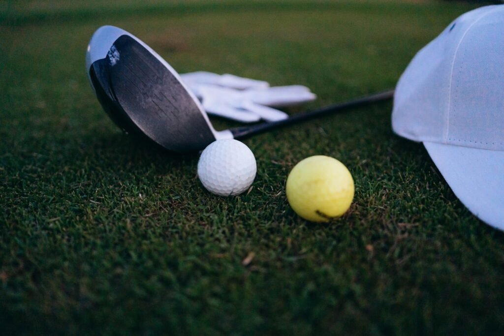 A golf driver, two golf balls, a glove, and a cap on the grass