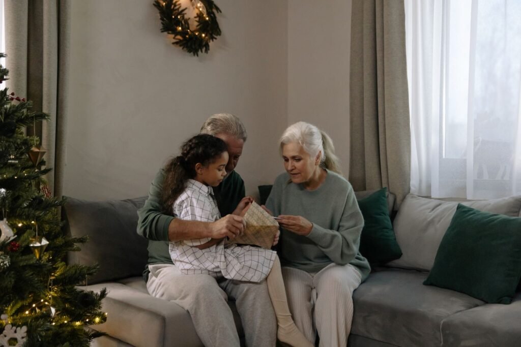 Grandparents and granddaughter opening a Christmas gift together on the sofa by the tree