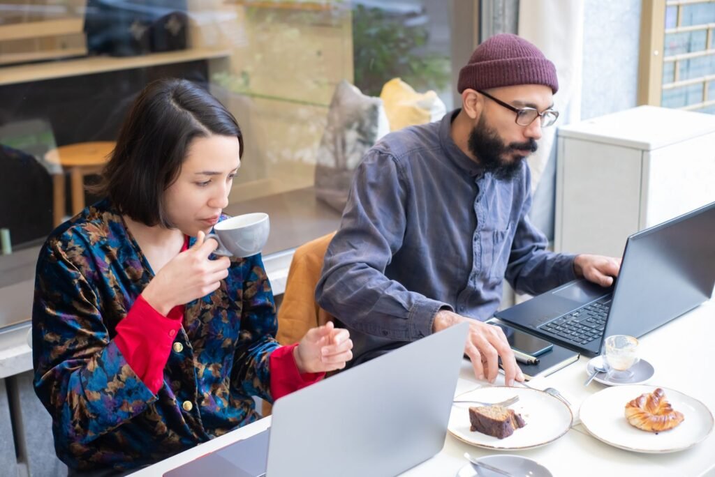 Two adults working on laptops in a contemporary café, enjoying coffee and pastries