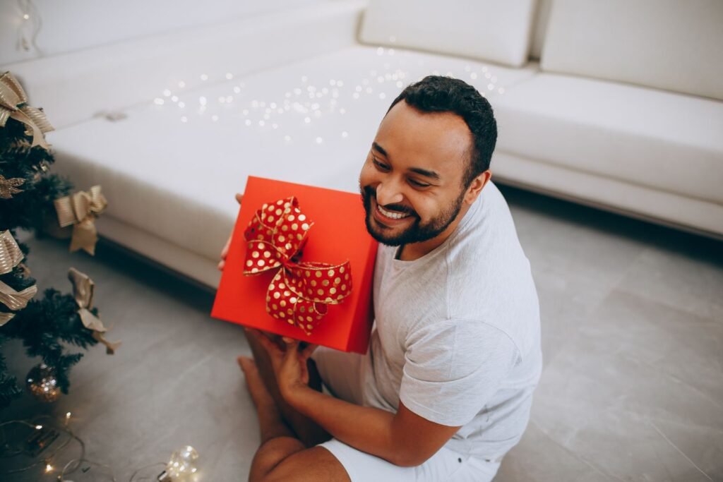 Smiling man sitting at home holding a red Christmas gift box with a big bow