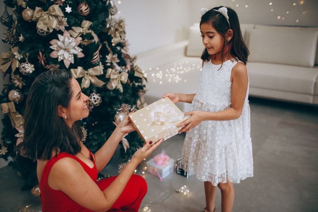 Daughter handing her mother a wrapped Christmas gift by a decorated tree