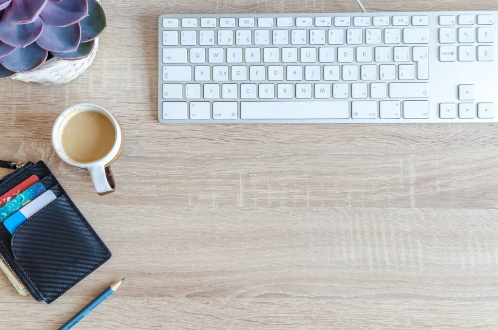 Top view of a tidy wooden desk with a keyboard, a cup of coffee, a wallet, a pencil, and a small succulent