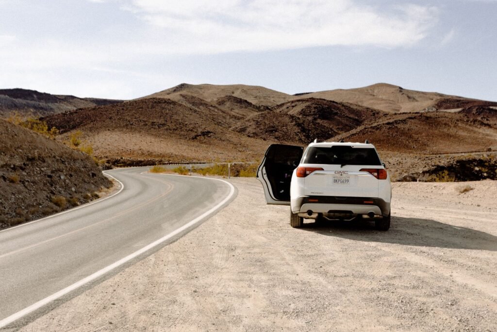 White SUV parked beside a winding desert road on a road trip under a clear sky