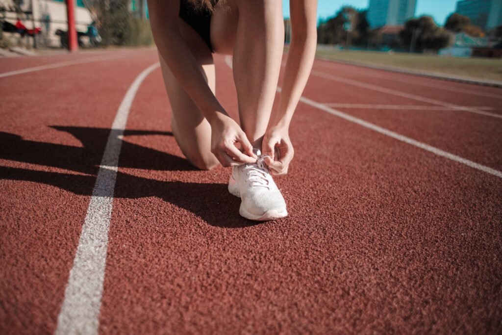 A runner tying her white sneakers on a red running track