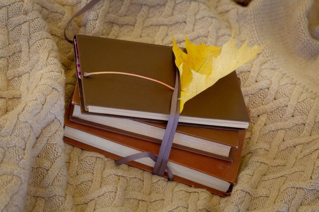 Stack of books with a yellow leaf on a knitted blanket