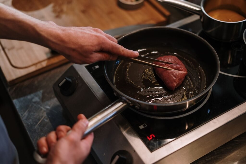 Steak searing in a skillet on a stovetop with tongs