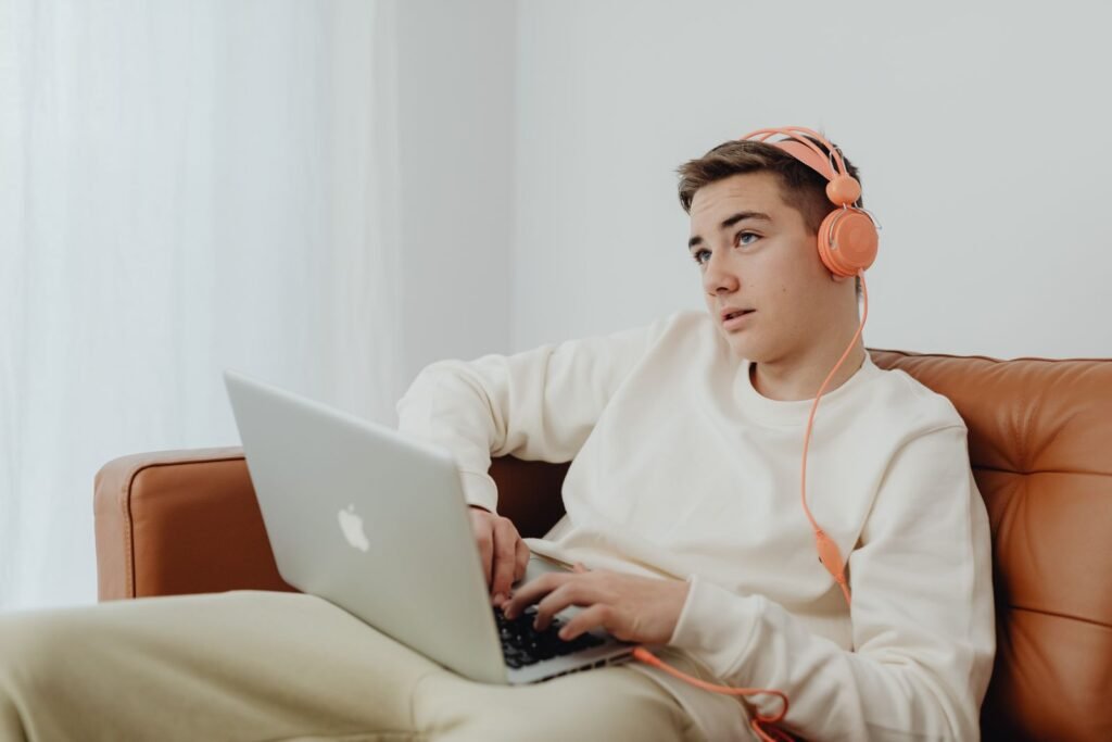 Teenage boy wearing headphones and using a laptop on a sofa