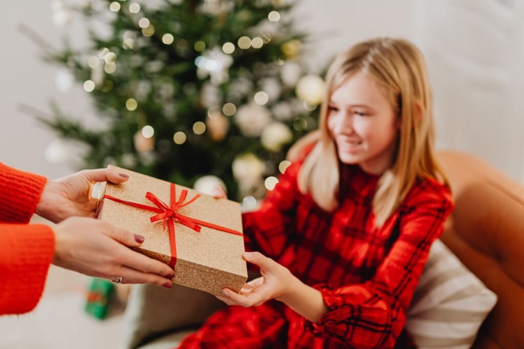 Smiling teenage girl receiving a wrapped Christmas gift by a decorated tree