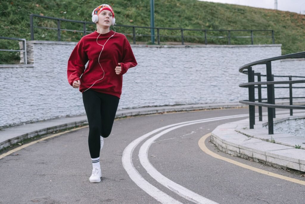 A woman in a red pullover jogging on a curved path while listening to music