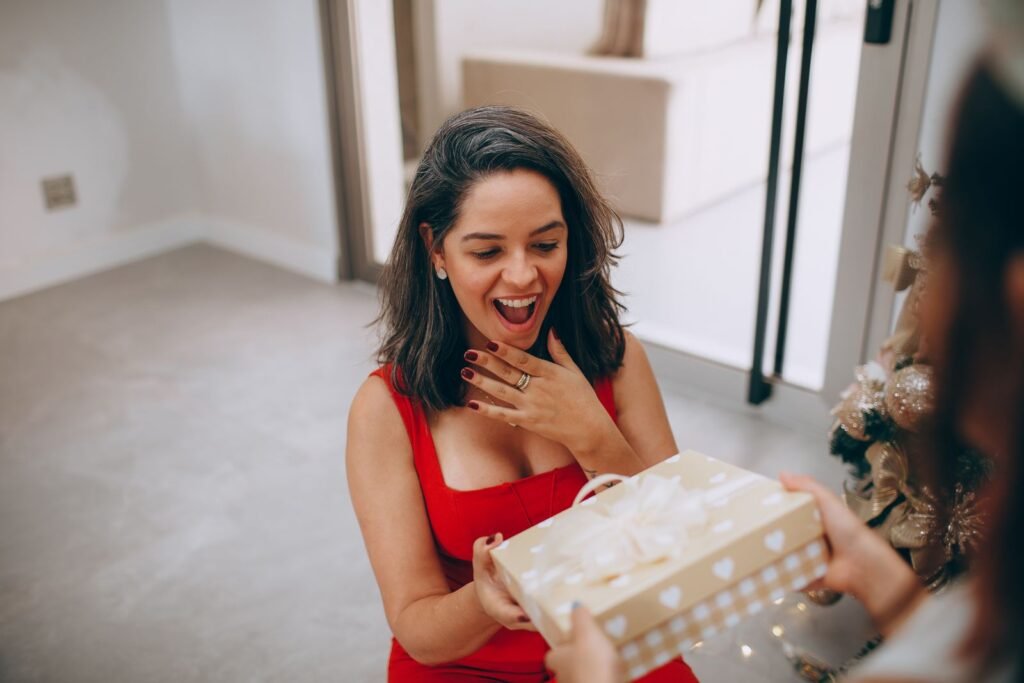 Smiling woman in a red dress opening a wrapped Christmas gift at home