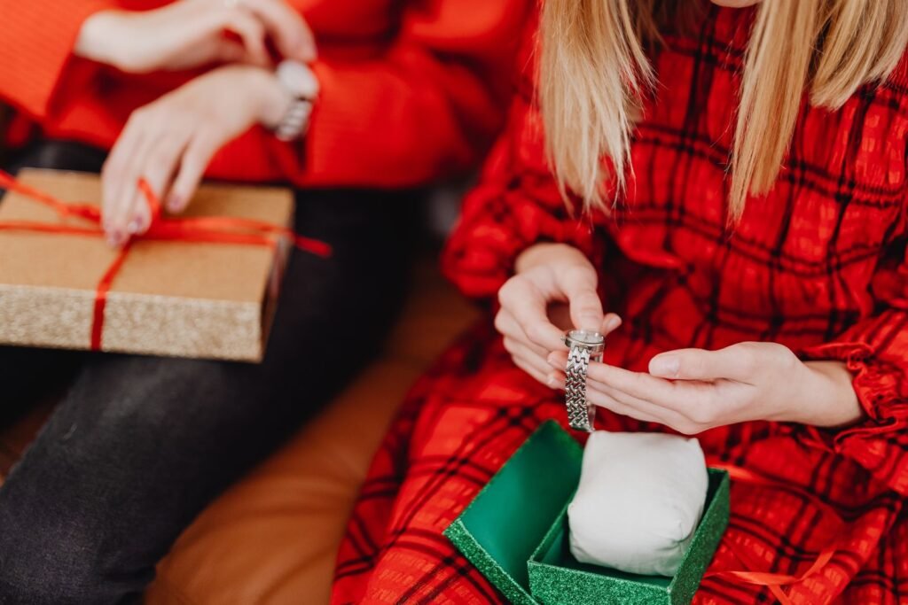 Woman in a red plaid dress lifting a piece of jewelry out of a green gift box during the holidays